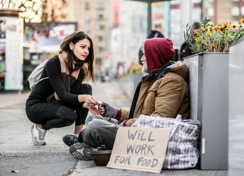 Mladá žena dáva peniaze žobrákovi bez domova, ktorý sedí v meste.