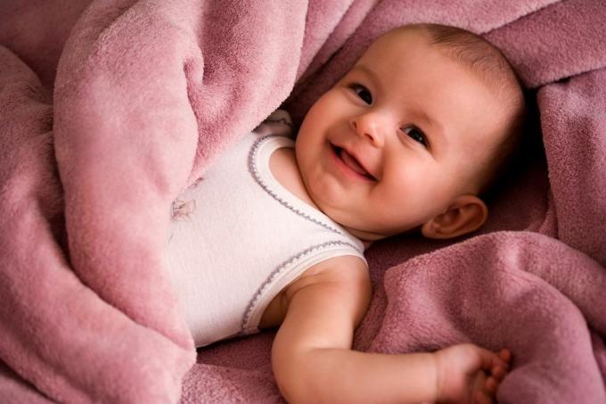 Portrét bábätka v bielej košeli v štýle tanku s úsmevom a zabalené v jemnej ružovej deke
