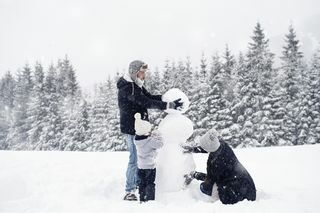 trojčlenná rodina stavia snehuliaka na snehu