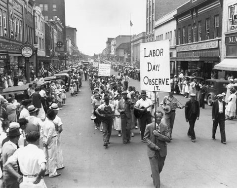 prehliadka Sviatku práce v roku 1934 s ľuďmi, ktorí kráčajú po ulici a držia značky, pretože dav sa pozerá z chodníkov