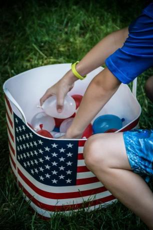 dieťa vyberá malé červené, biele a modré vodné balóniky z vane s americkou vlajkou na ňom