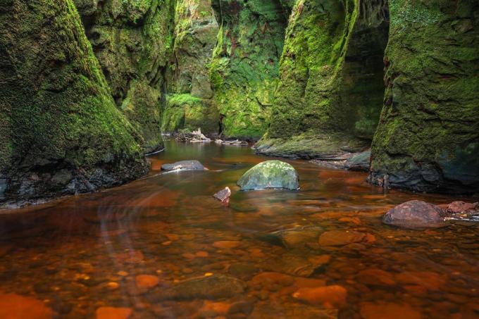 Krvavo červená rieka v zelenej rokline. Devil's Pulpit, Finnich Glen, blízko Killearn, Škótsko, Spojené kráľovstvo