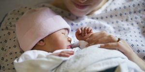 novonarodené dievčatko v ružovej čiapočke zavinuté v deke s matkou pri pohľade od brady nadol v nemocničnom plášti, ktorý ju drží