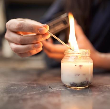 plodina anonymná žena s horiacou zápalkou zapálenie aromatickej sviečky v sklenenej nádobe umiestnenej na mramorovom stole doma