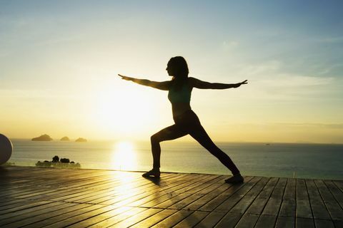 Žena robí jogu pri mori pri západe slnka