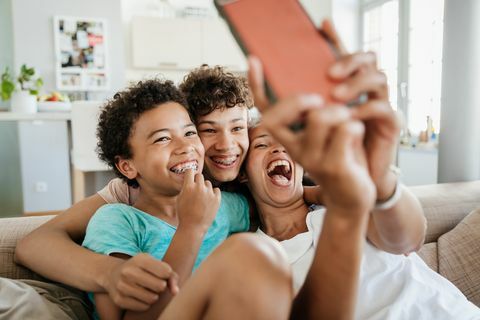 slobodná mama, ktorá sa baví so svojimi dvoma synmi doma, sedia na gauči a berú selfie na svojom smartfóne