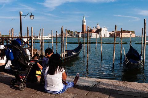 Turisti sedia na zemi v Benátkach, zatiaľ čo sa pozerajú na kostol San Giorgio