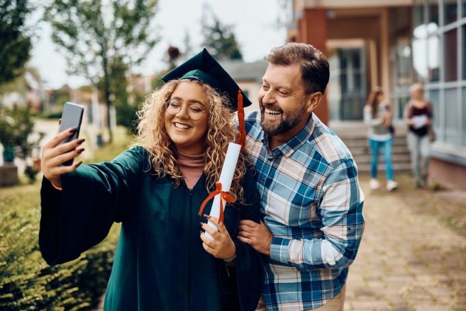 šťastná absolventka univerzity a jej otec sa zabávajú pri fotení selfie s chytrým telefónom