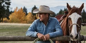 Kevin costner v Yellowstone vedľa koňa opierajúceho sa o plot s povrazom v rukách, na sebe vyblednutú modrú džínsovú košeľu a béžový kovbojský klobúk