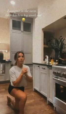 jessie james decker robí rýchly tréning nôh v kuchyni, zatiaľ čo pečie recept na lasagne z kuchárskej knihy