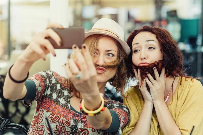 dve priateľky, ktoré si držia vlasy na tvári, aby vyzerali, že majú bradu a fúzy, a robia si z toho selfie