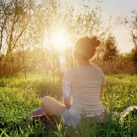 mladá žena sediaca v pozícii jogy a užíva si západ slnka v prírode