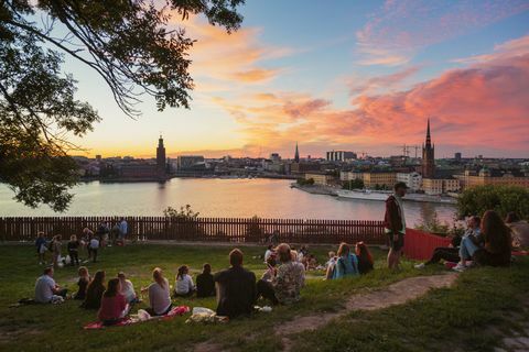 Ľudia, ktorí majú piknik v parku s panorámou Štokholmu pri západe slnka, Švédsko