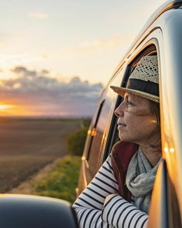 žena po 40-tke sa kochá pohľadom na krajinu zo svojho karavanu, vyzerá spokojne a uvoľnene