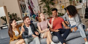 mladá žena hovorí niečo svojim štyrom priateľom, dvom mužom a dvom ženám, pričom ich rozosmieva, keď spolu sedí doma na gauči